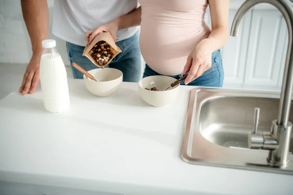 Cropped view of pregnant couple making cereals with milk in kitchen — Stock Photo