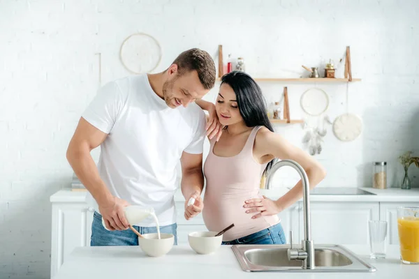 Счастливая беременная жена и муж делает хлопья с молоком на кухне — стоковое фото
