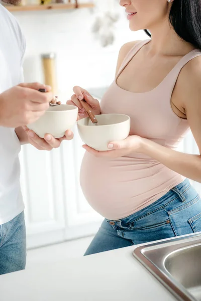 Vista recortada de la esposa embarazada y el marido comiendo cereales con leche en la cocina - foto de stock