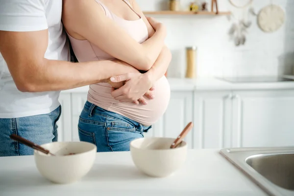 Partial view of pregnant couple hugging in kitchen with cereals in bowls — Stock Photo