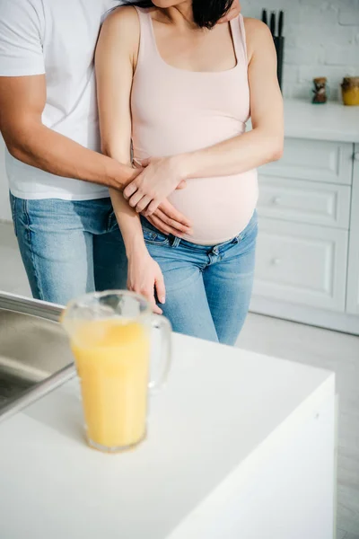 Обрізаний вид чоловіка торкається живота вагітної жінки на кухні з апельсиновим соком — стокове фото