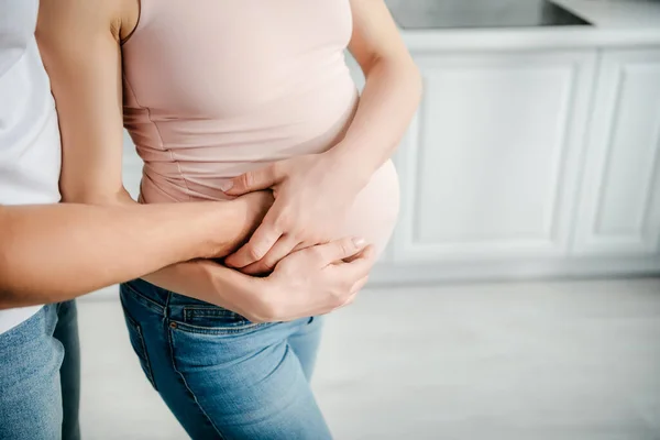 Vista parcial del marido tocando vientre de la esposa embarazada en la cocina - foto de stock