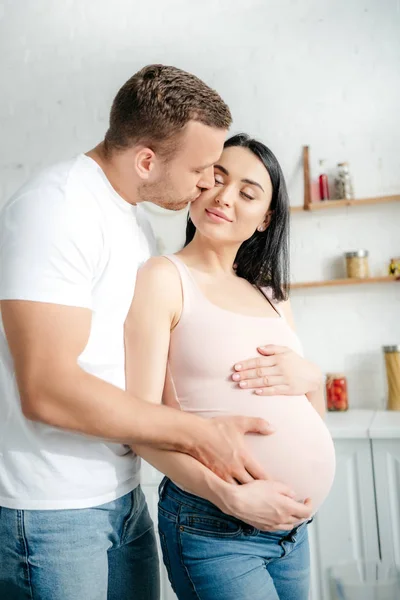 Mari tendre toucher le ventre de la femme enceinte et l'embrasser dans la cuisine — Photo de stock