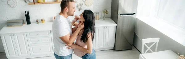 Tiro panorámico de marido feliz abrazando a su esposa embarazada en la cocina - foto de stock