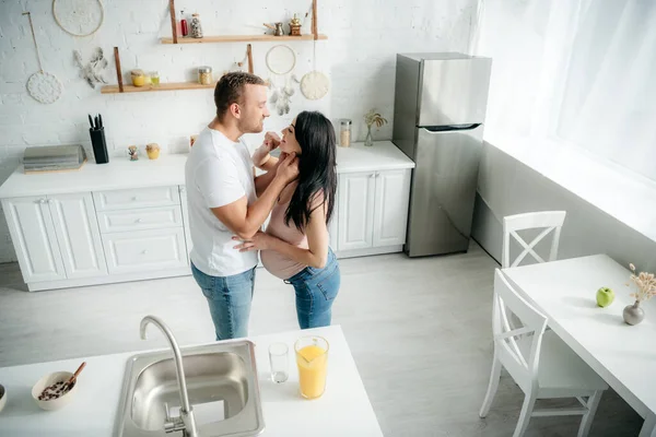 Счастливая беременная семья обнимается на кухне с апельсиновым соком — стоковое фото