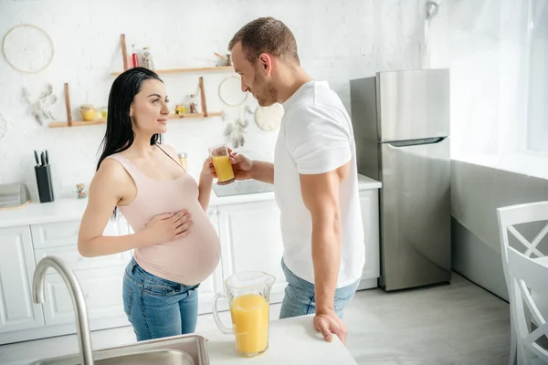 Счастливая беременная жена и муж пьют апельсиновый сок на кухне — стоковое фото