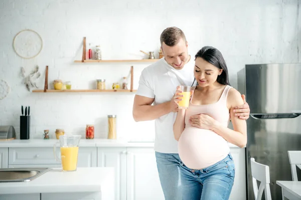 Happy beautiful pregnant couple holding orange juice in kitchen — Stock Photo
