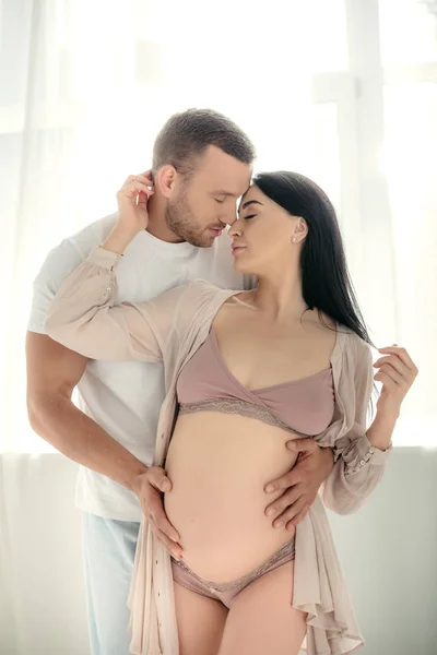 Marido tierno guapo abrazando a su hermosa esposa embarazada - foto de stock