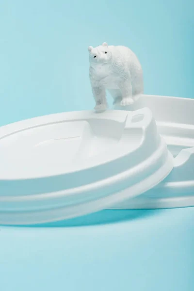 Brinquedo urso polar em tampas de café de plástico em fundo azul, conceito de bem-estar animal — Fotografia de Stock