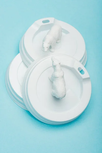 Top view of toy polar bears on plastic coffee lids on blue background, ecological problem concept — Stock Photo