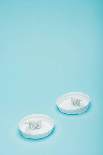 White toy polar bears on plastic coffee lids on blue background, animal welfare concept — Stock Photo