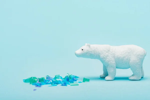 Orso polare giocattolo accanto a pezzi di plastica su sfondo blu, concetto di benessere degli animali — Foto stock