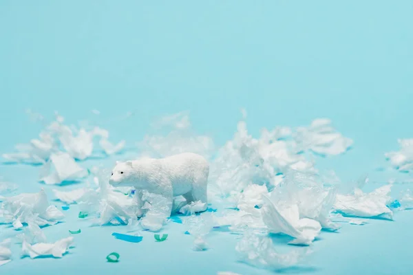 Weißer Spielzeug-Eisbär mit Plastikmüll auf blauem Hintergrund, Tierschutzkonzept — Stockfoto