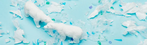 Panoramic shot of toy polar bears with polyethylene and plastic pieces on blue background, animal welfare concept — Stock Photo