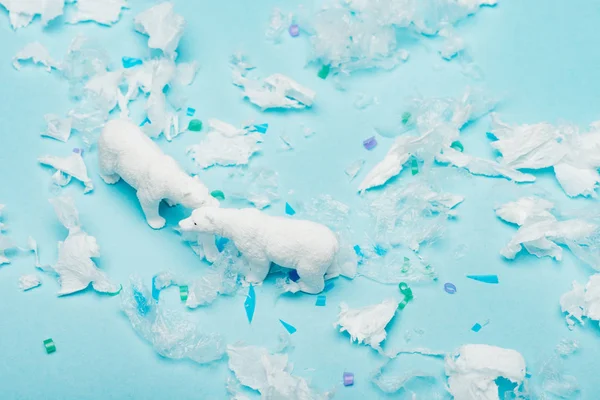 Високий кут зору іграшкових полярних ведмедів з пластиковими шматочками на синьому фоні, концепція забруднення навколишнього середовища — стокове фото