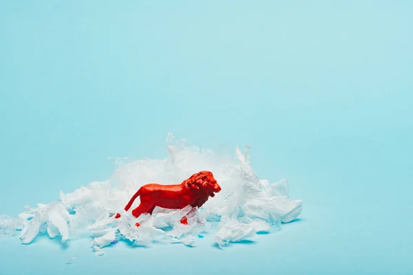 Leão de brinquedo vermelho com lixo de plástico no fundo azul, conceito de bem-estar animal — Fotografia de Stock