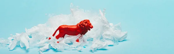 Панорамний знімок червоного іграшкового лева з пластиковим сміттям на синьому фоні, концепція добробуту тварин — стокове фото