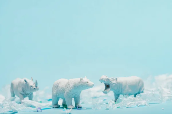 Brinquedos brancos de hipopótamo, rinoceronte e urso com lixo de plástico no fundo azul, conceito de bem-estar animal — Fotografia de Stock