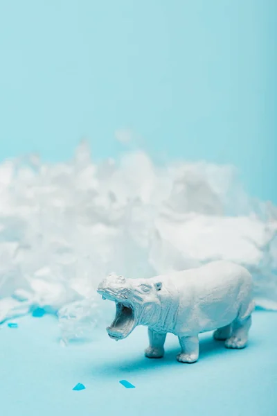 Selective focus of hippopotamus toy with plastic garbage on blue background, animal welfare concept — Stock Photo