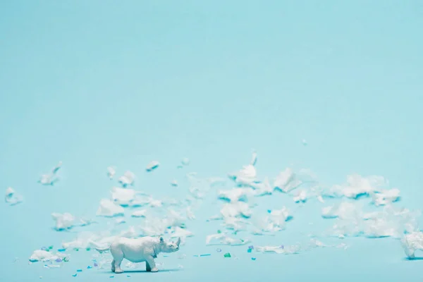 Juguete blanco rinoceronte y basura plástica sobre fondo azul, concepto de contaminación ambiental - foto de stock