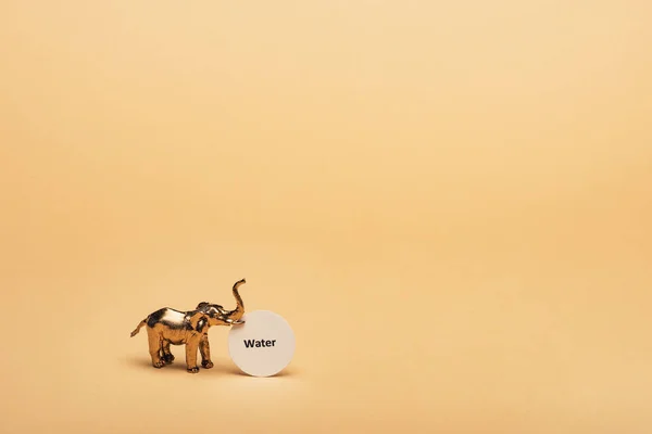 Elefante de juguete dorado con letras de agua en la tarjeta sobre fondo amarillo, concepto de escasez de agua - foto de stock