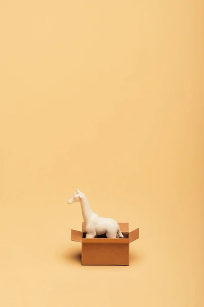 Girafe jouet blanc dans une boîte en carton sur fond jaune, concept de bien-être animal — Photo de stock