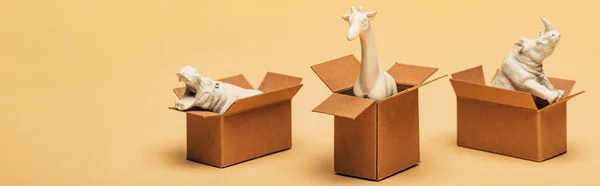 Foto panorámica de juguete hipopótamo, rinoceronte y jirafa en cajas de cartón sobre fondo amarillo, concepto de bienestar animal - foto de stock