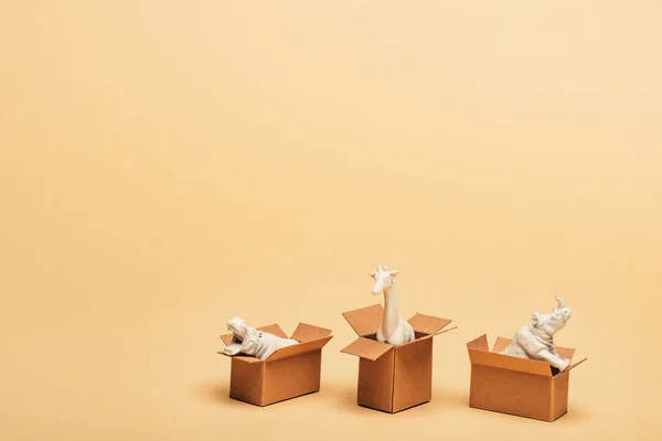 White toy hippopotamus, rhinoceros and giraffe in cardboard boxes on yellow background, animal welfare concept — Stock Photo