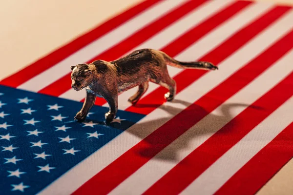Tigre de juguete dorado con sombra en la bandera americana, concepto de bienestar animal - foto de stock