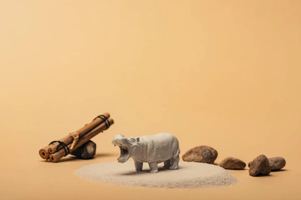 White toy hippopotamus with stones and wooden sticks on yellow background, animal welfare concept — Stock Photo