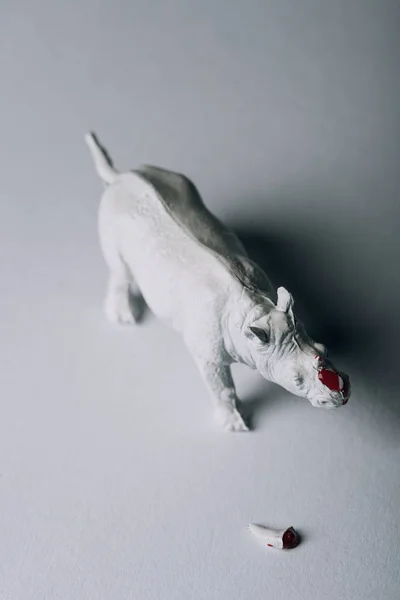 Vista superior de cuerno con sangre y rinoceronte de juguete sobre fondo gris, caza del concepto de cuerno - foto de stock