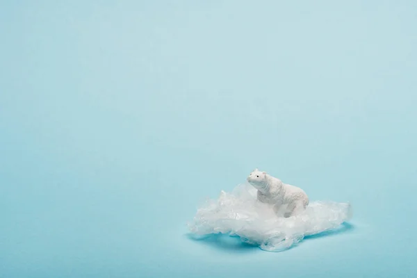 Іграшковий білий ведмідь на пластиковій упаковці на синьому фоні, концепція забруднення навколишнього середовища — стокове фото