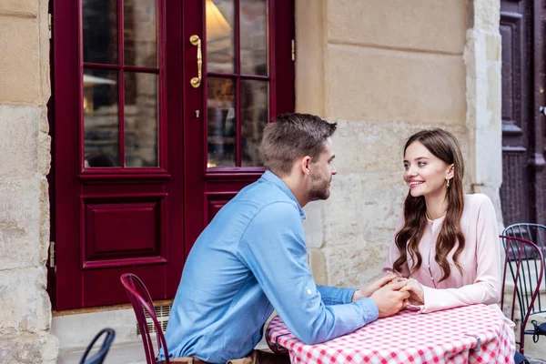 Щаслива молода пара тримає руки і дивиться один на одного, сидячи у вуличному кафе — стокове фото