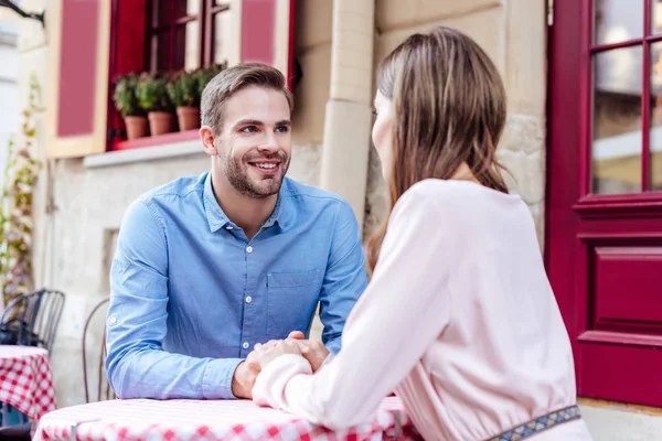 Glücklicher junger Mann hält Hand seiner Freundin, während er am Tisch in einem Straßencafé sitzt — Stockfoto