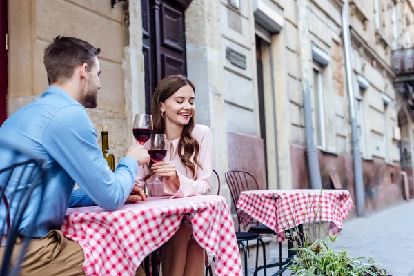 Jolie jeune femme cliquetis verres de vin rouge avec petit ami tout en étant assis dans la rue café — Photo de stock