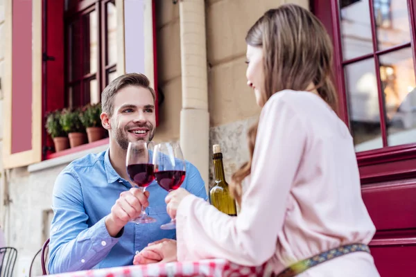Heureux jeune couple cliquetis verres à vin tandis que assis à la table dans la rue café — Photo de stock