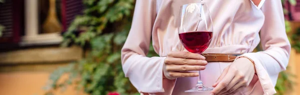 Vista recortada de la mujer sosteniendo copa de vino tinto, plano panorámico - foto de stock