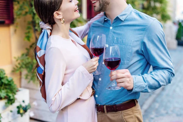 Cropped view of happy couple looking at each other while holding glasses of red wine — Stock Photo