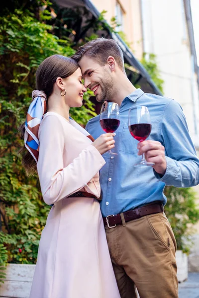 Счастливая пара обнимается, стоя лицом к лицу и держа бокалы красного вина — стоковое фото