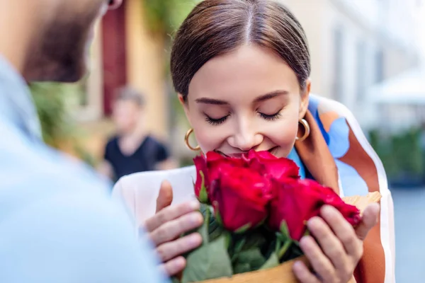 Vista recortada de hombre joven presentando ramo de rosas a novia feliz en la calle - foto de stock