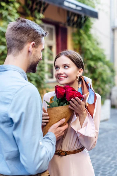 Joven hombre presentando ramo de rosas a feliz novia en la calle - foto de stock