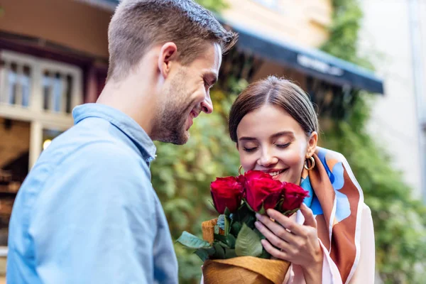 Uomo sorridente che presenta mazzo di rose a ragazza felice su strada — Foto stock