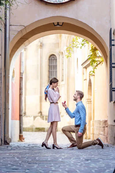 Vista lateral del hombre haciendo de pie sobre la rodilla y hacer propuesta de matrimonio a la novia en la calle - foto de stock