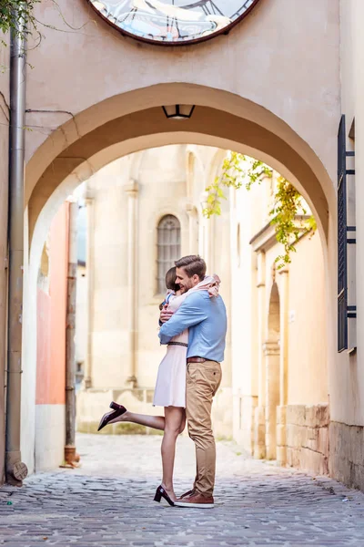 Ein paar glückliche junge Touristen umarmen sich, während sie unter einem Bogen auf der Straße stehen — Stockfoto