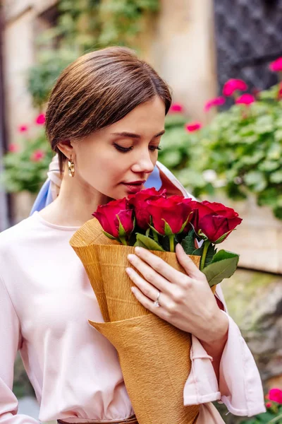 Bella, ragazza sognante godendo sapore di rose rosse mentre tiene bouquet — Foto stock