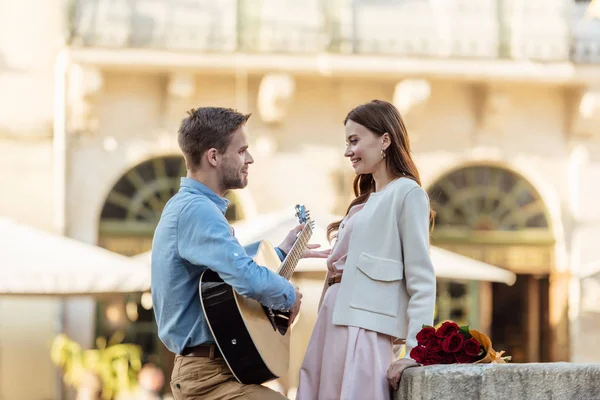 Bel homme jouant de la guitare acoustique pour belle petite amie sur steet — Photo de stock