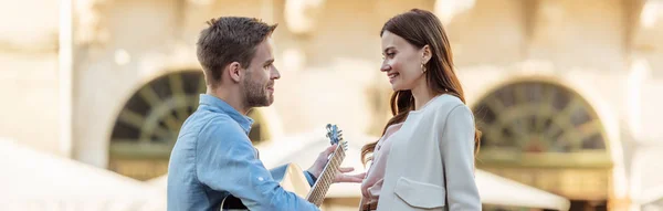 Plano panorámico de hombre guapo tocando la guitarra para hermosa novia en la calle - foto de stock