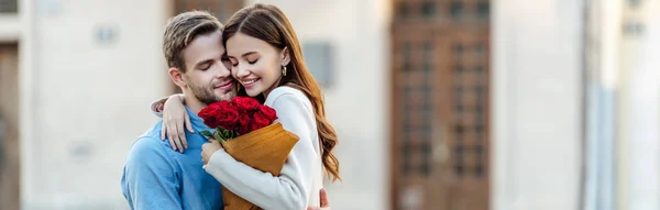 Panoramaaufnahme eines glücklichen Mädchens, das seinen Freund umarmt, während es einen Strauß Rosen in der Hand hält — Stockfoto