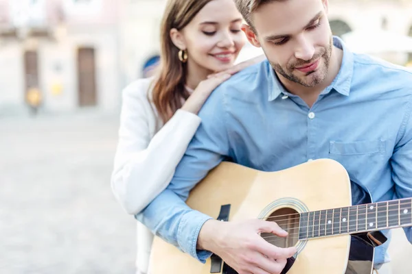 Selektiver Fokus eines jungen Mannes, der neben seiner glücklichen Freundin Akustikgitarre spielt — Stockfoto