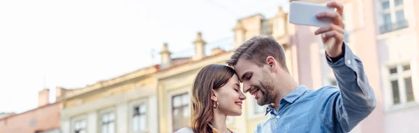 Plan panoramique de l'homme heureux prenant selfie avec petite amie souriante — Photo de stock